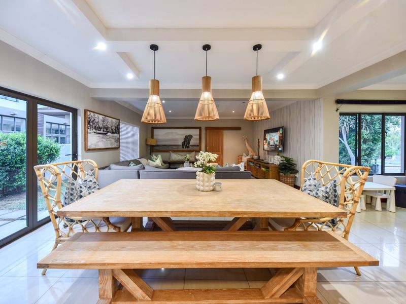 Spacious open-plan living and dining area featuring tiled floors, recessed ceiling details, modern pendant lighting, and large sliding glass doors providing ample natural light.
