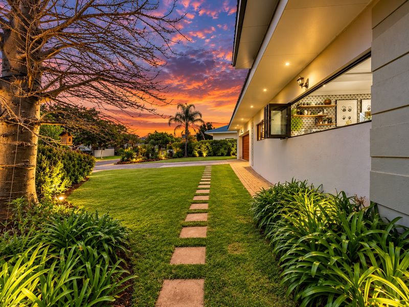 A beautifully landscaped front garden featuring a stone paver walkway, exterior lighting, and a modern bi-fold window opening onto the lawn at sunset.