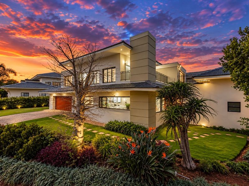 A stunning double-storey residential property featuring a modern facade, integrated garage, balcony, and beautifully landscaped garden at twilight.