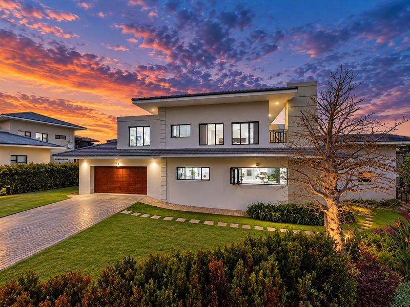 Modern double-story residence featuring a paved driveway, integrated double garage, and a well-maintained landscaped garden under a dramatic sunset sky.
