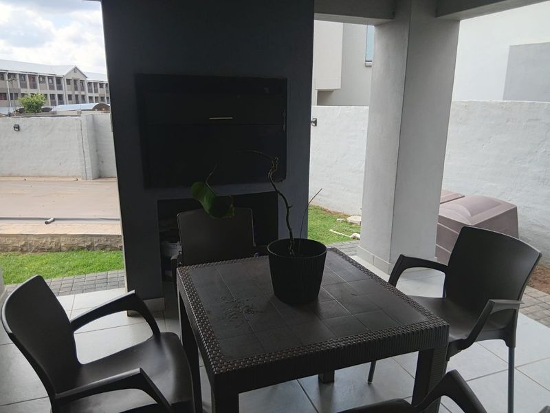 A covered patio area featuring a built-in braai, tiled flooring, and structural concrete pillars, providing a functional outdoor entertainment space.
