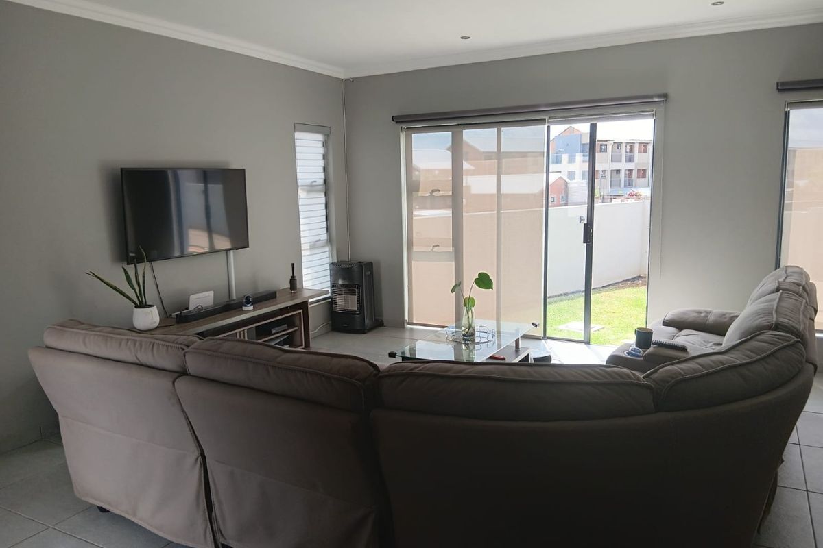 A well-lit living room featuring tiled flooring, recessed downlights, and large sliding glass doors providing access to the rear garden area.