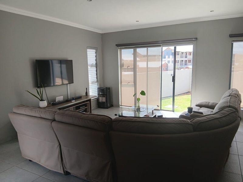 A well-lit living room featuring tiled flooring, recessed downlights, and large sliding glass doors providing access to the rear garden area.