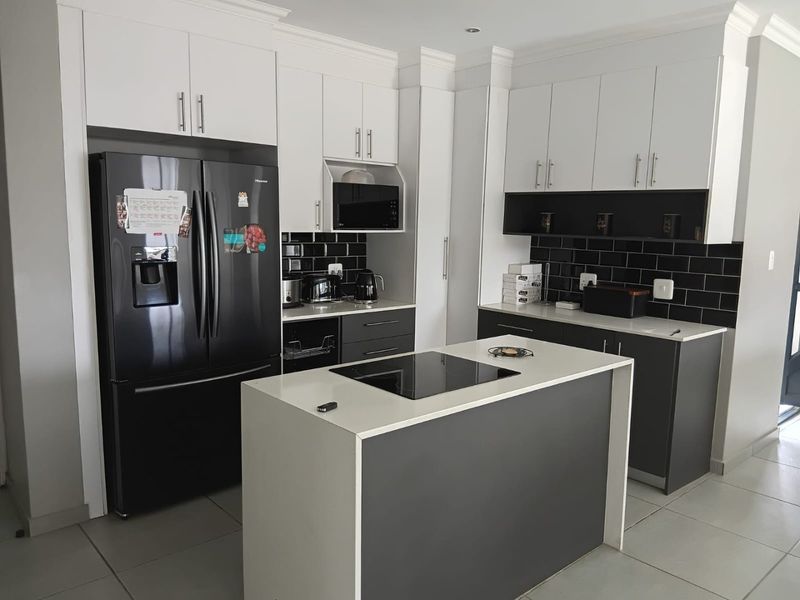 Modern kitchen featuring two-tone cabinetry, a central island with an integrated induction cooktop, stone countertops, and a stylish black subway tile backsplash.