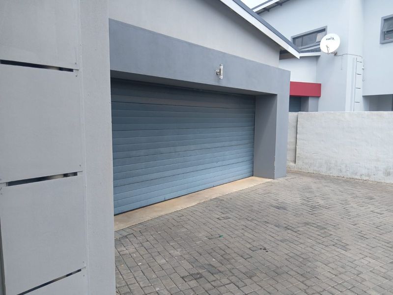 A modern double garage with a grey automated door and paved driveway, featuring clean architectural lines and exterior wall lighting.