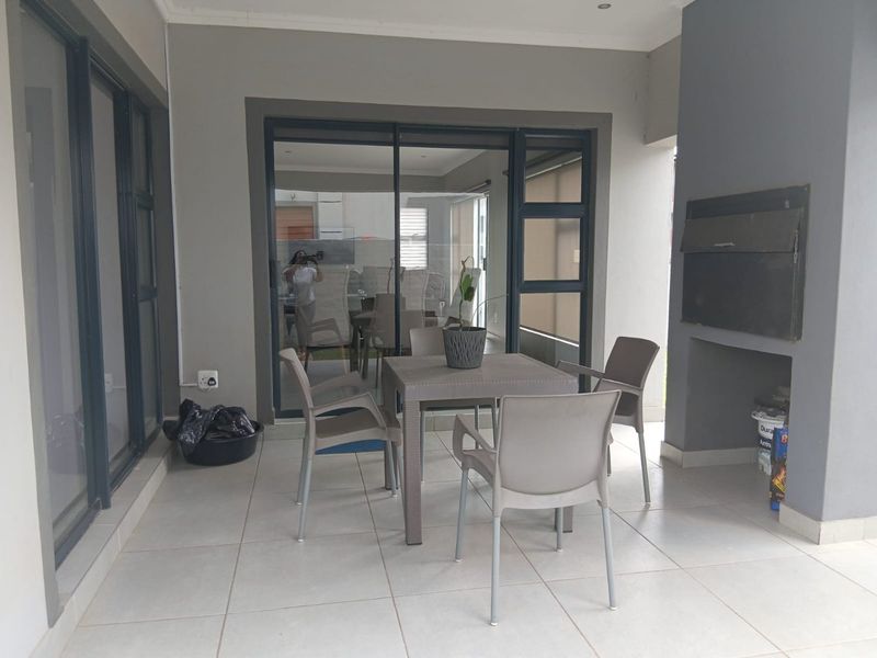 Covered patio area featuring tiled flooring, recessed lighting, and a built-in braai, providing a seamless transition to the interior living space via sliding doors.