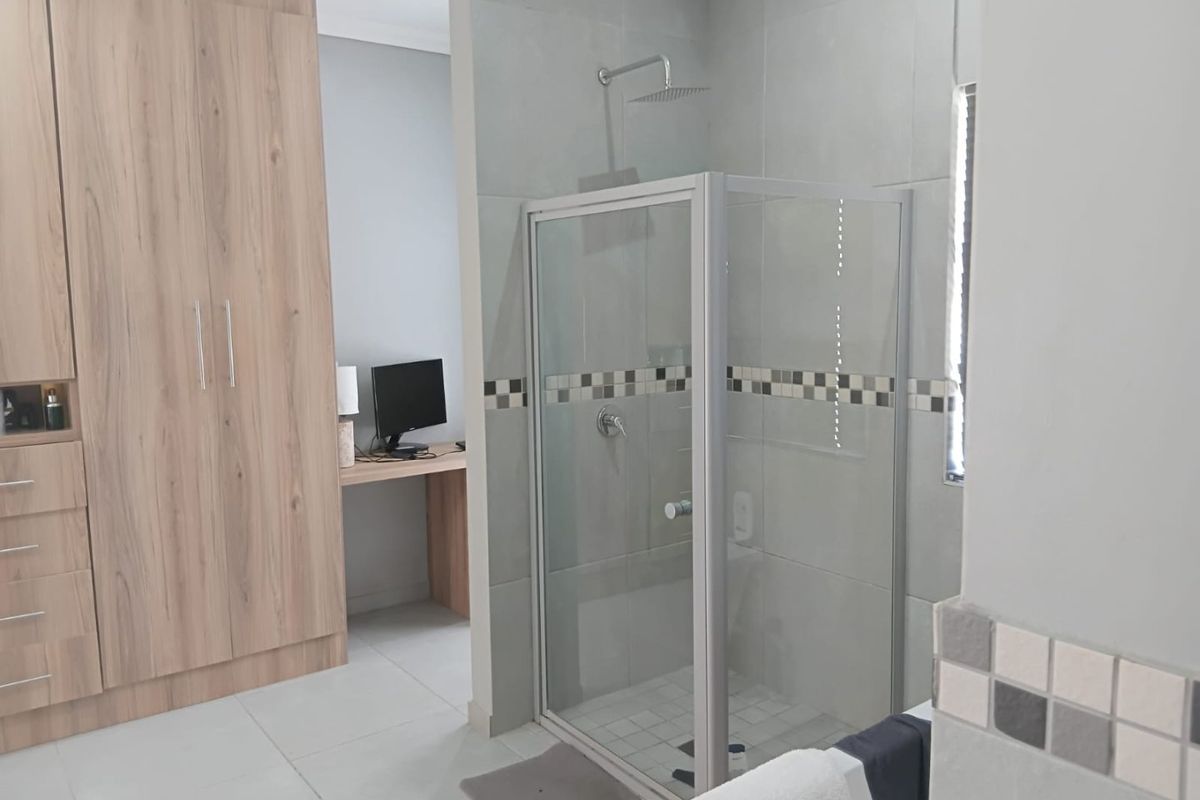 Bedroom featuring a modern built-in wardrobe and an en-suite shower area with contemporary grey tiling and a rain shower head.