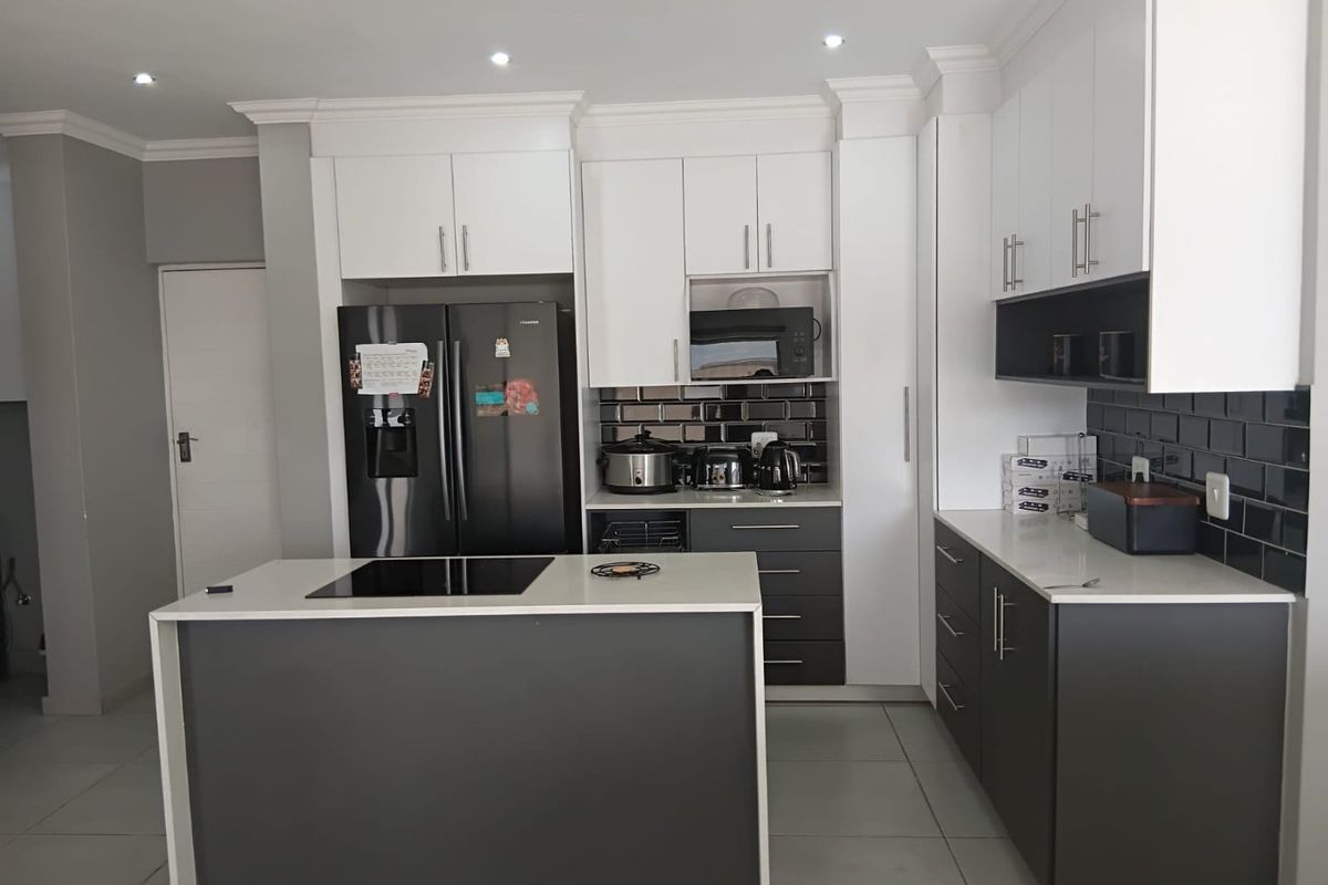 Modern kitchen featuring two-tone cabinetry, a central island with an integrated induction cooktop, quartz countertops, and a stylish black subway tile backsplash.