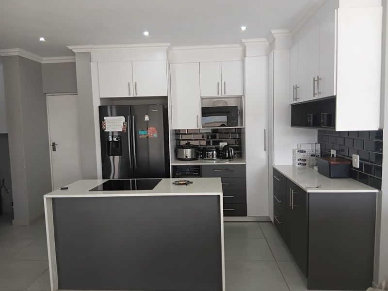 Modern kitchen featuring two-tone cabinetry, a central island with an integrated induction cooktop, quartz countertops, and a stylish black subway tile backsplash.