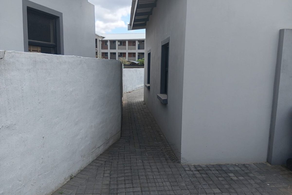 A paved side walkway between two exterior building walls with a boundary wall enclosure.