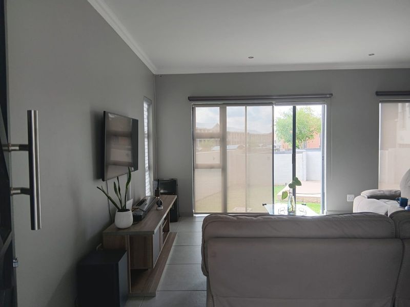 A well-maintained living room featuring neutral grey walls, tiled flooring, and large sliding glass doors that provide access to the rear garden area.
