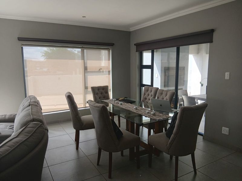 A well-lit dining area featuring neutral tiled flooring, large windows with roller blinds, and sliding glass doors providing access to the outdoor patio.