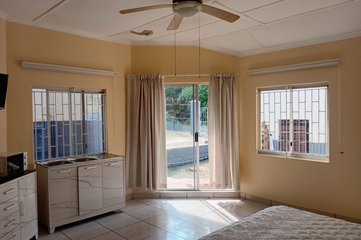 Bedroom featuring tiled floors, a ceiling fan, and a small kitchenette area with a double sink, leading out to an exterior patio.