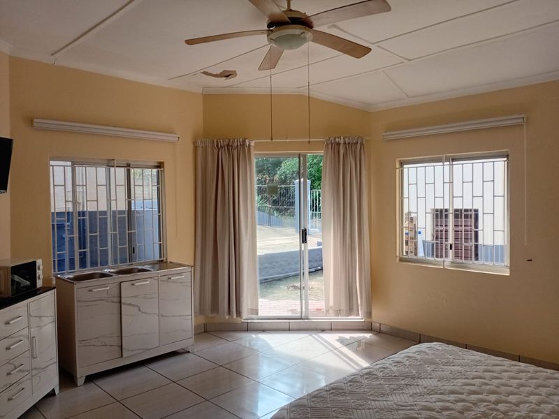 Bedroom featuring tiled floors, a ceiling fan, and a small kitchenette area with a double sink, leading out to an exterior patio.