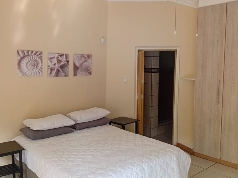 A bedroom featuring tiled flooring, a ceiling fan, and built-in cupboards, with direct access to an en-suite bathroom.