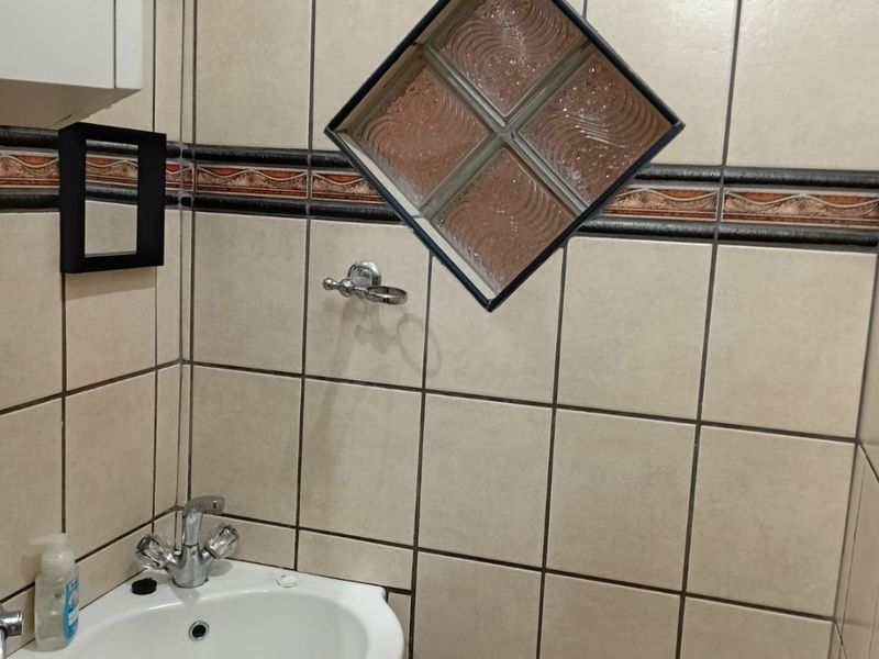 A compact bathroom featuring a pedestal basin with chrome mixer tap, tiled walls with a decorative border, and a unique diamond-shaped glass block window.