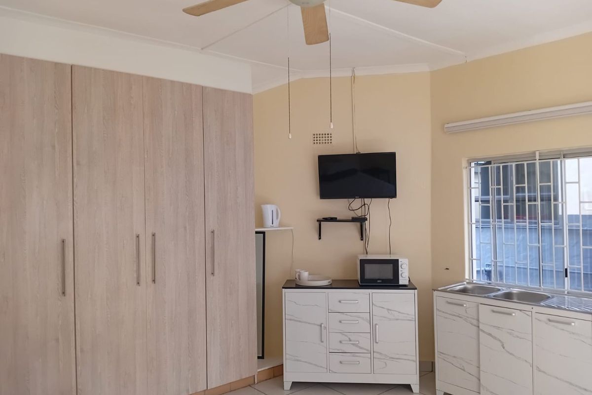 Bedroom featuring built-in cupboards, a ceiling fan, tiled flooring, and a small kitchenette area with a sink and security bars on the window.