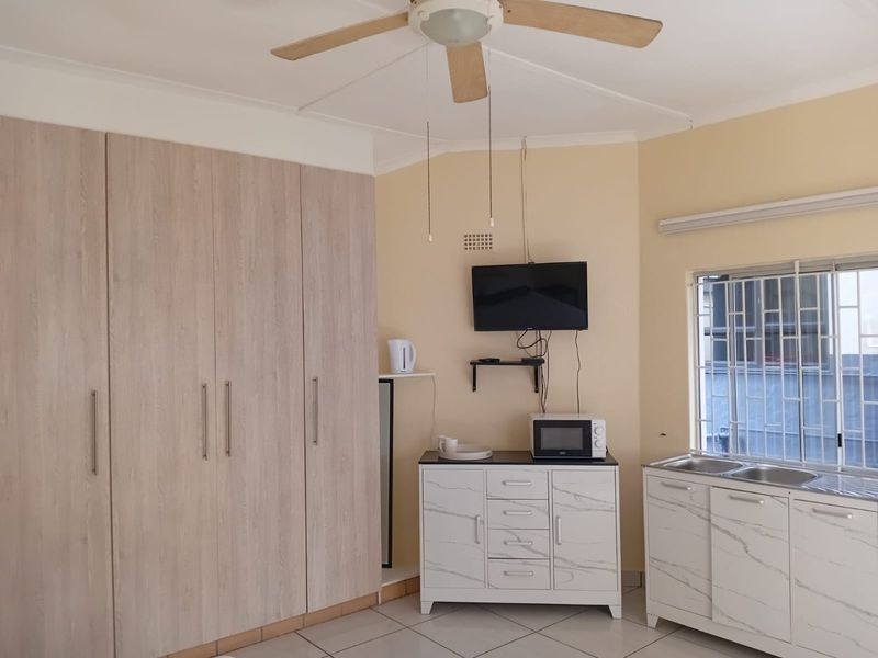 Bedroom featuring built-in cupboards, a ceiling fan, tiled flooring, and a small kitchenette area with a sink and security bars on the window.