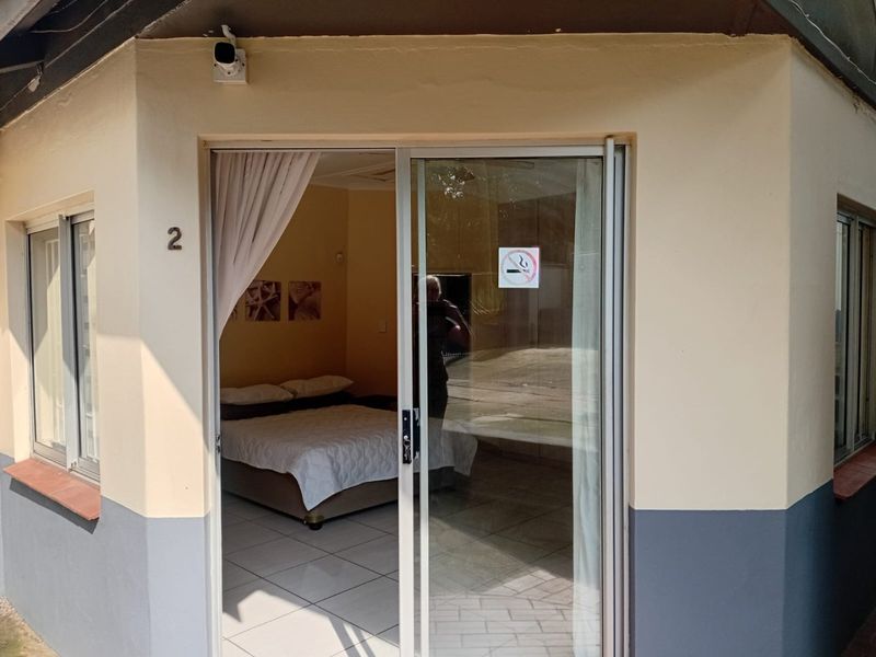 Exterior view of an apartment entrance featuring a sliding glass door, security camera, and tiled flooring leading into the bedroom.