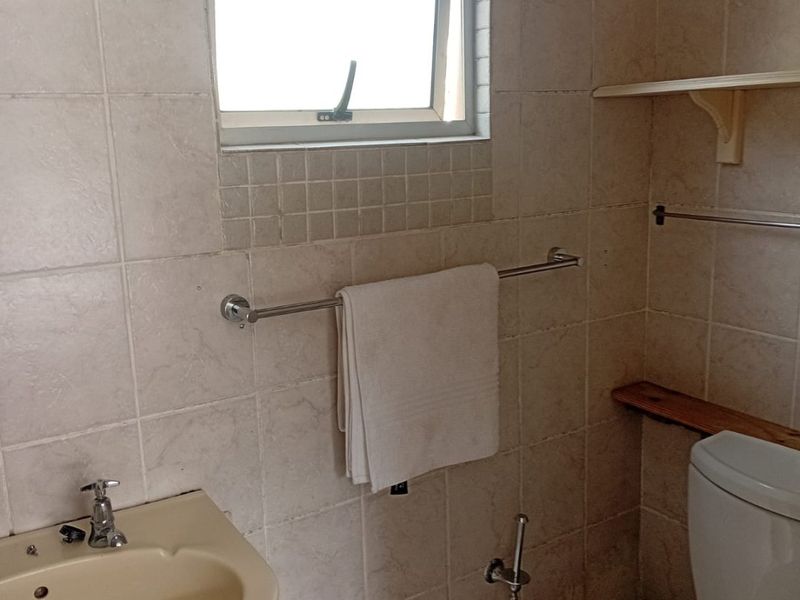 A compact bathroom featuring tiled walls and flooring, a pedestal basin, and a standard toilet, requiring cosmetic updates to modernize the space.
