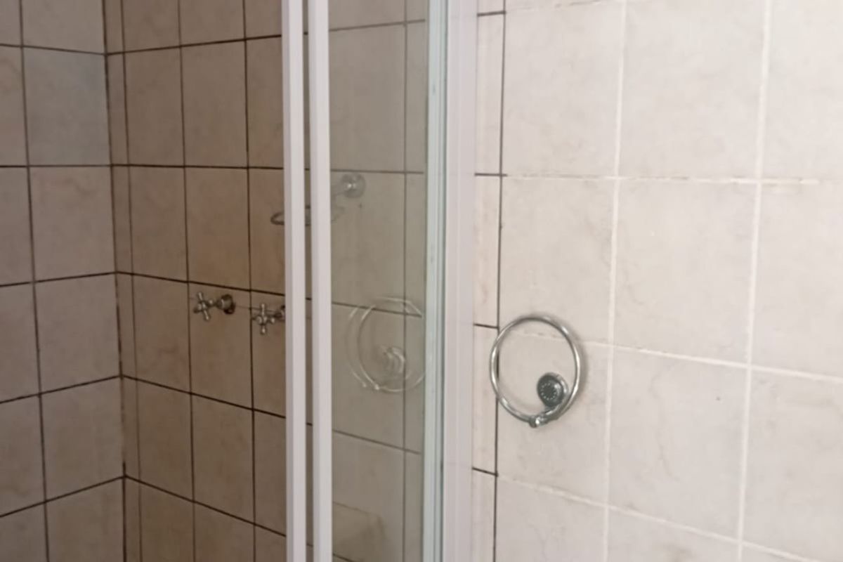 A functional bathroom featuring a shower enclosure with tiled walls and a wall-mounted basin, presenting an opportunity for modernization.