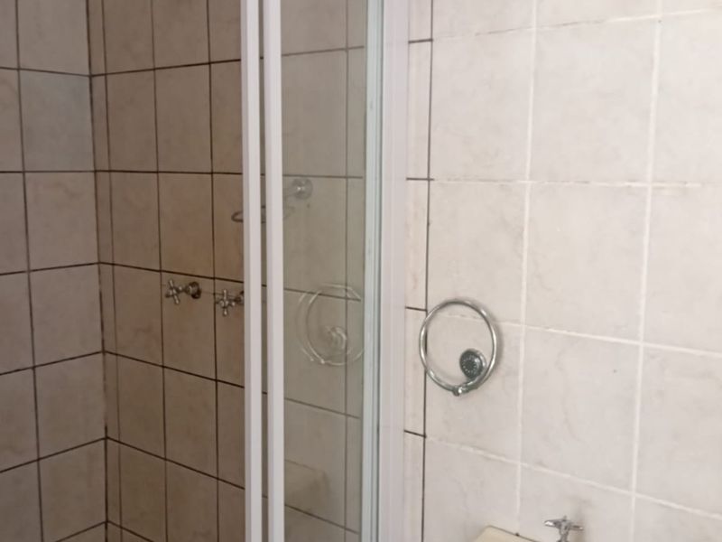 A functional bathroom featuring a shower enclosure with tiled walls and a wall-mounted basin, presenting an opportunity for modernization.