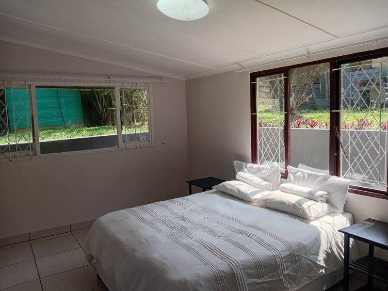 A bedroom featuring tiled flooring, large windows with security bars, and natural light, offering a functional space with potential for modern updates.