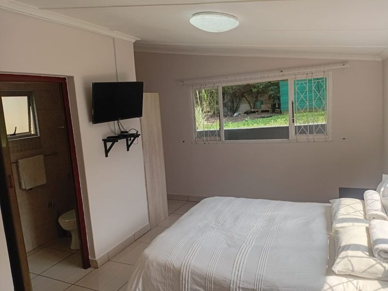 A bedroom featuring tiled flooring, security bars on the window, and an adjoining en-suite bathroom.