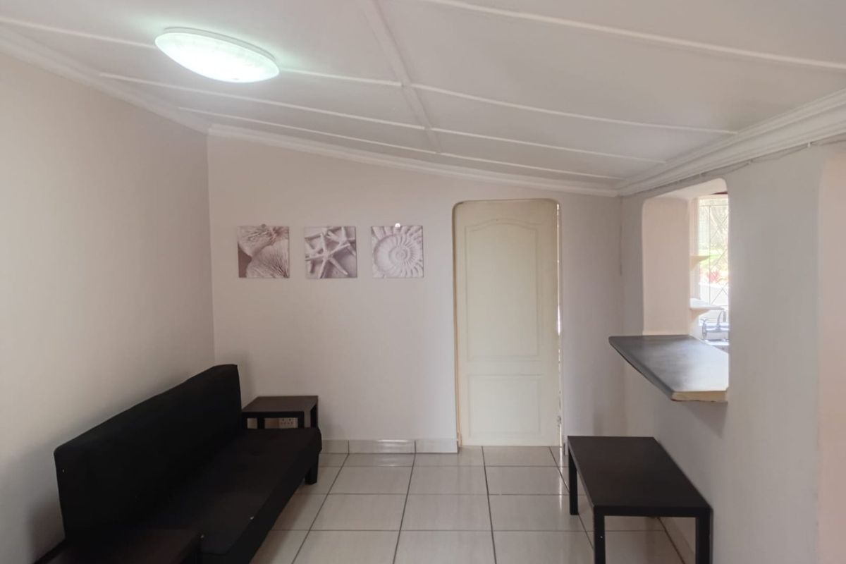 A living area featuring tiled flooring, a breakfast bar pass-through to the kitchen, and a panelled ceiling.