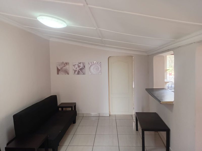 A living area featuring tiled flooring, a breakfast bar pass-through to the kitchen, and a panelled ceiling.