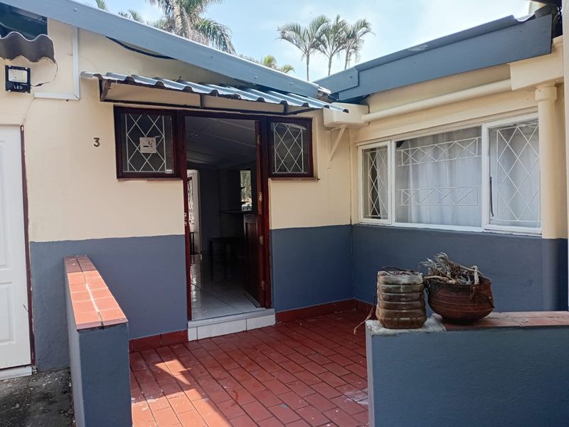 Front entrance of the apartment featuring a tiled patio area, security gate, and exterior wall finishes.