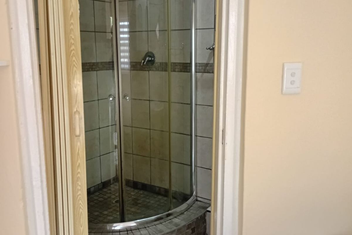 A compact bathroom featuring a curved glass shower enclosure with tiled surround and flooring, accessed via a folding door.