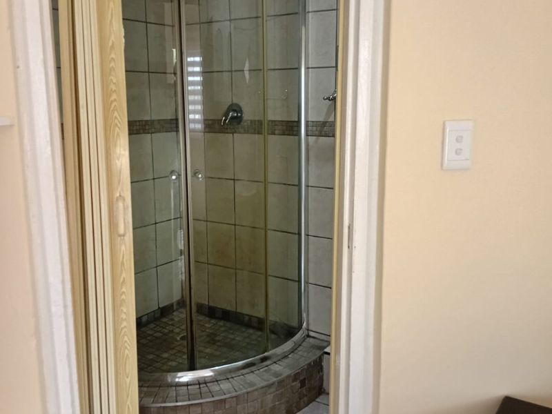 A compact bathroom featuring a curved glass shower enclosure with tiled surround and flooring, accessed via a folding door.