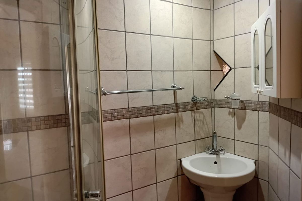 A compact bathroom featuring a corner pedestal basin, shower enclosure, and tiled walls with a decorative border.