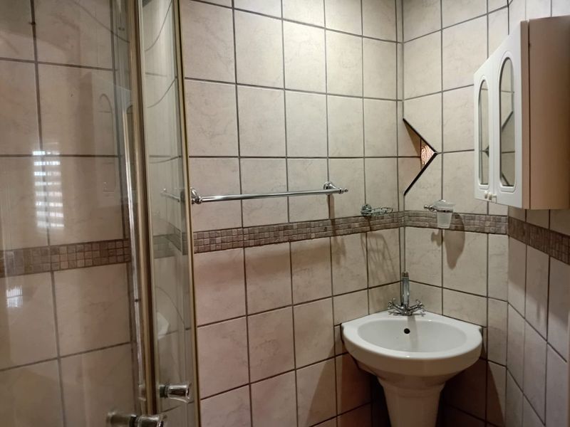 A compact bathroom featuring a corner pedestal basin, shower enclosure, and tiled walls with a decorative border.