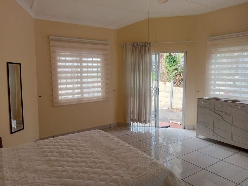 A bright bedroom featuring tiled flooring, built-in vanity cabinetry, and a sliding glass door providing direct access to the exterior.