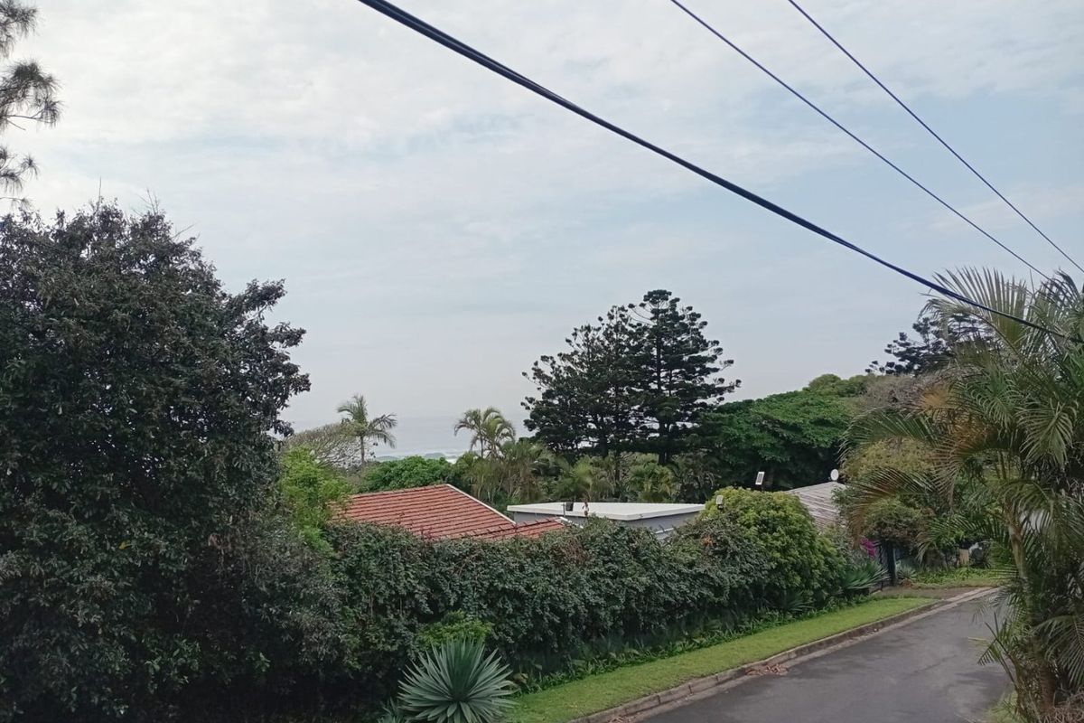 A street-level view showing the neighborhood approach, surrounding greenery, and glimpses of nearby residential rooftops.
