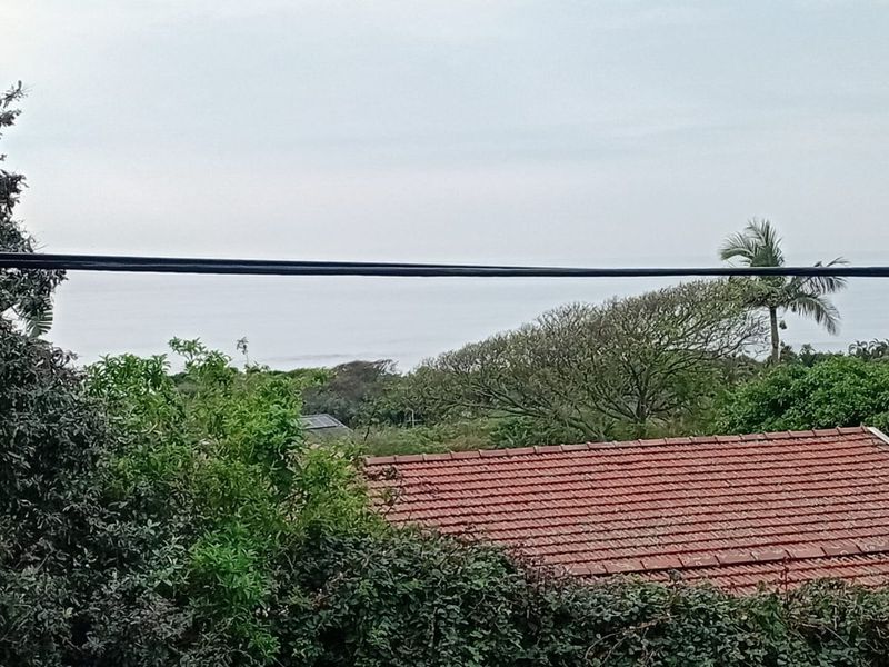 An elevated view overlooking a tiled roof with surrounding greenery and a distant ocean horizon.