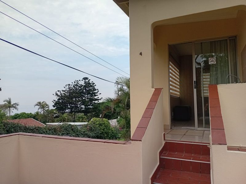 Exterior view of an apartment entrance featuring a tiled staircase, a sliding glass door, and a terrace area with surrounding greenery.