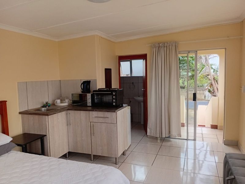 Open-plan studio apartment featuring a kitchenette with laminate countertops, tiled flooring, and direct access to an outdoor patio area.