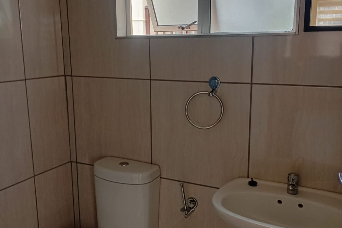 A functional bathroom featuring tiled walls and flooring, a pedestal basin, and a standard toilet with a top-hung window for ventilation.