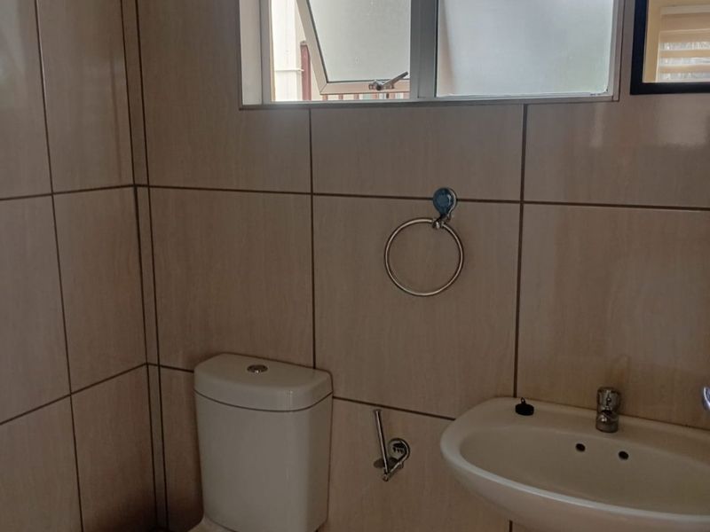 A functional bathroom featuring tiled walls and flooring, a pedestal basin, and a standard toilet with a top-hung window for ventilation.