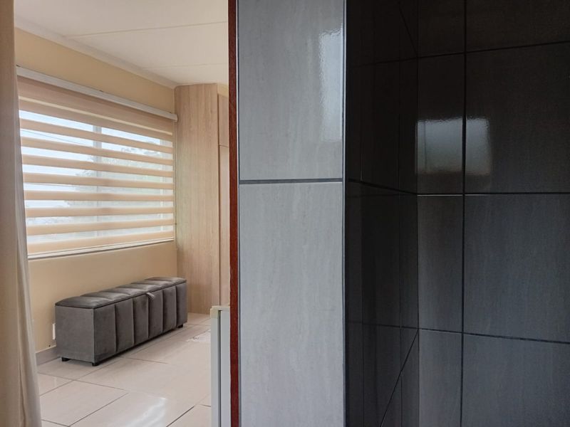 A bedroom featuring built-in cupboards, tiled flooring, and modern roller blinds, offering a clean and functional living space.