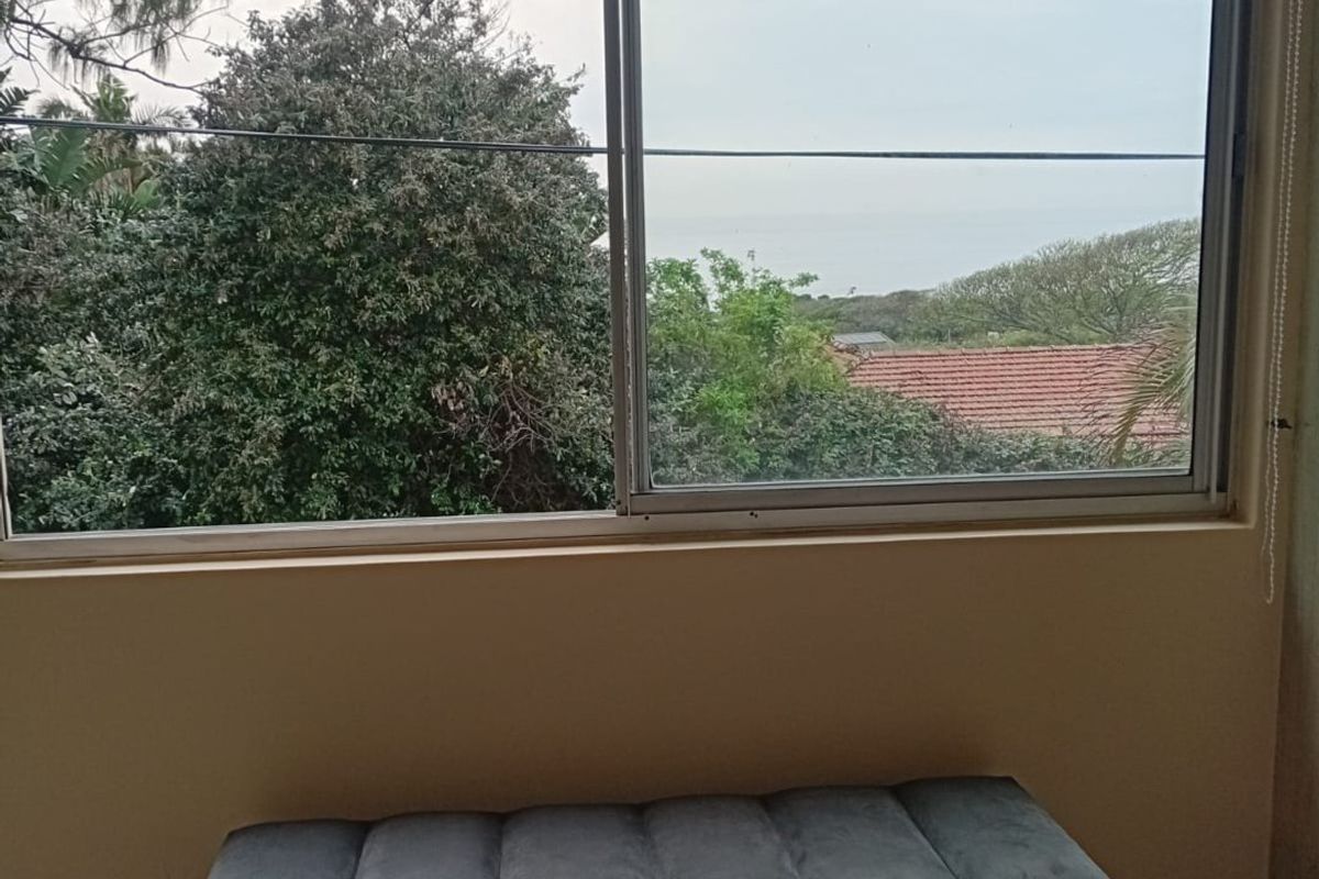 A bedroom interior featuring a large sliding window with a view of the surrounding greenery and distant ocean.