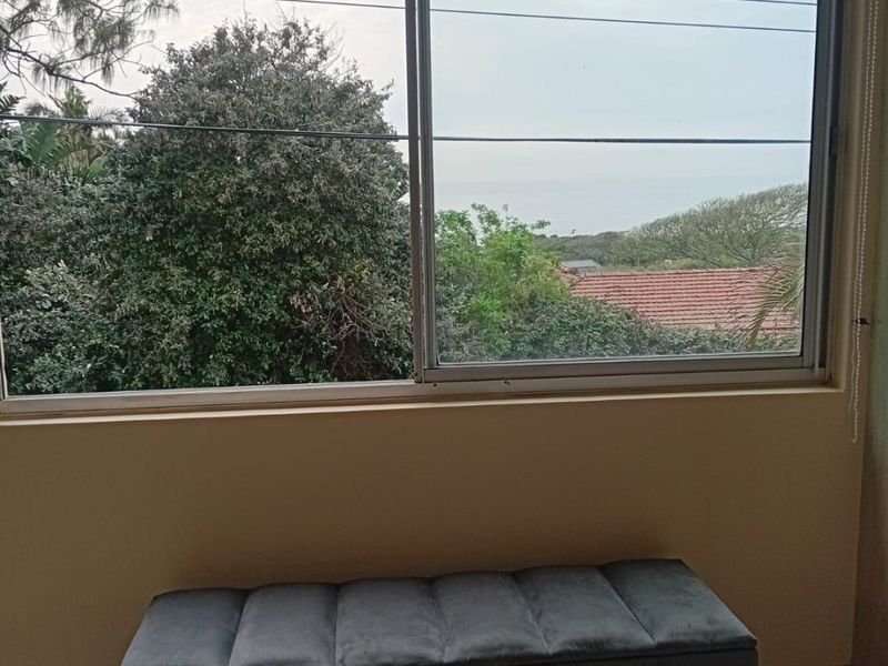 A bedroom interior featuring a large sliding window with a view of the surrounding greenery and distant ocean.