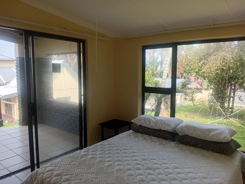 Bedroom featuring large windows and a sliding glass door leading to an outdoor patio area with garden views.