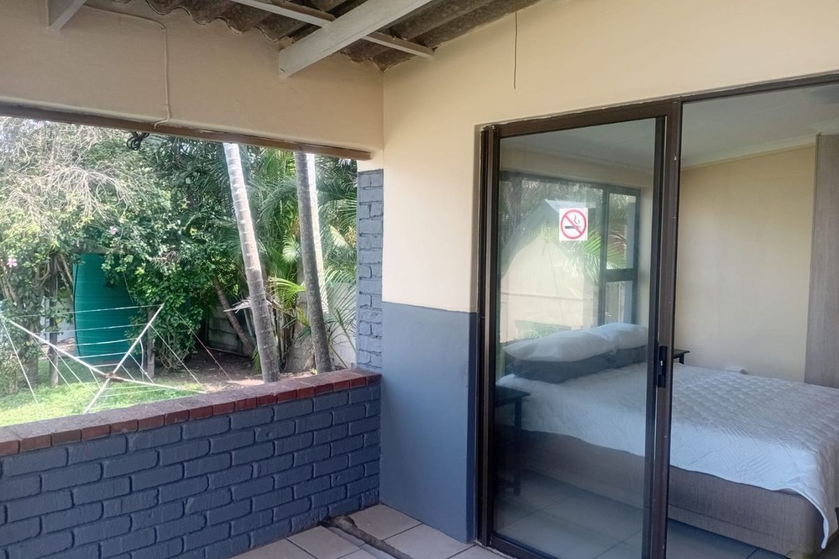 A covered patio area featuring a brick balustrade and sliding glass door access to the bedroom, overlooking a private garden space.