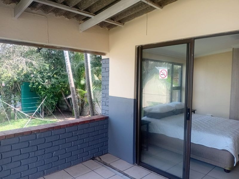 A covered patio area featuring a brick balustrade and sliding glass door access to the bedroom, overlooking a private garden space.