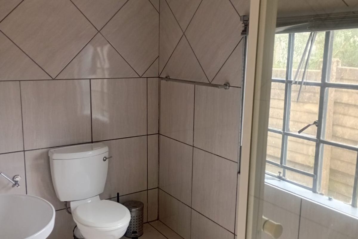 A functional bathroom featuring tiled walls and flooring, a pedestal basin, and a toilet, with natural light provided by a steel frame window.