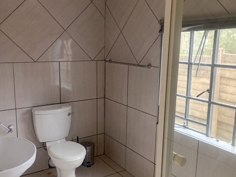 A functional bathroom featuring tiled walls and flooring, a pedestal basin, and a toilet, with natural light provided by a steel frame window.